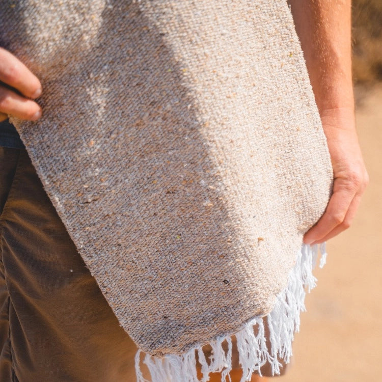 Person holding a textured woven blanket with fringes on a blurred natural background