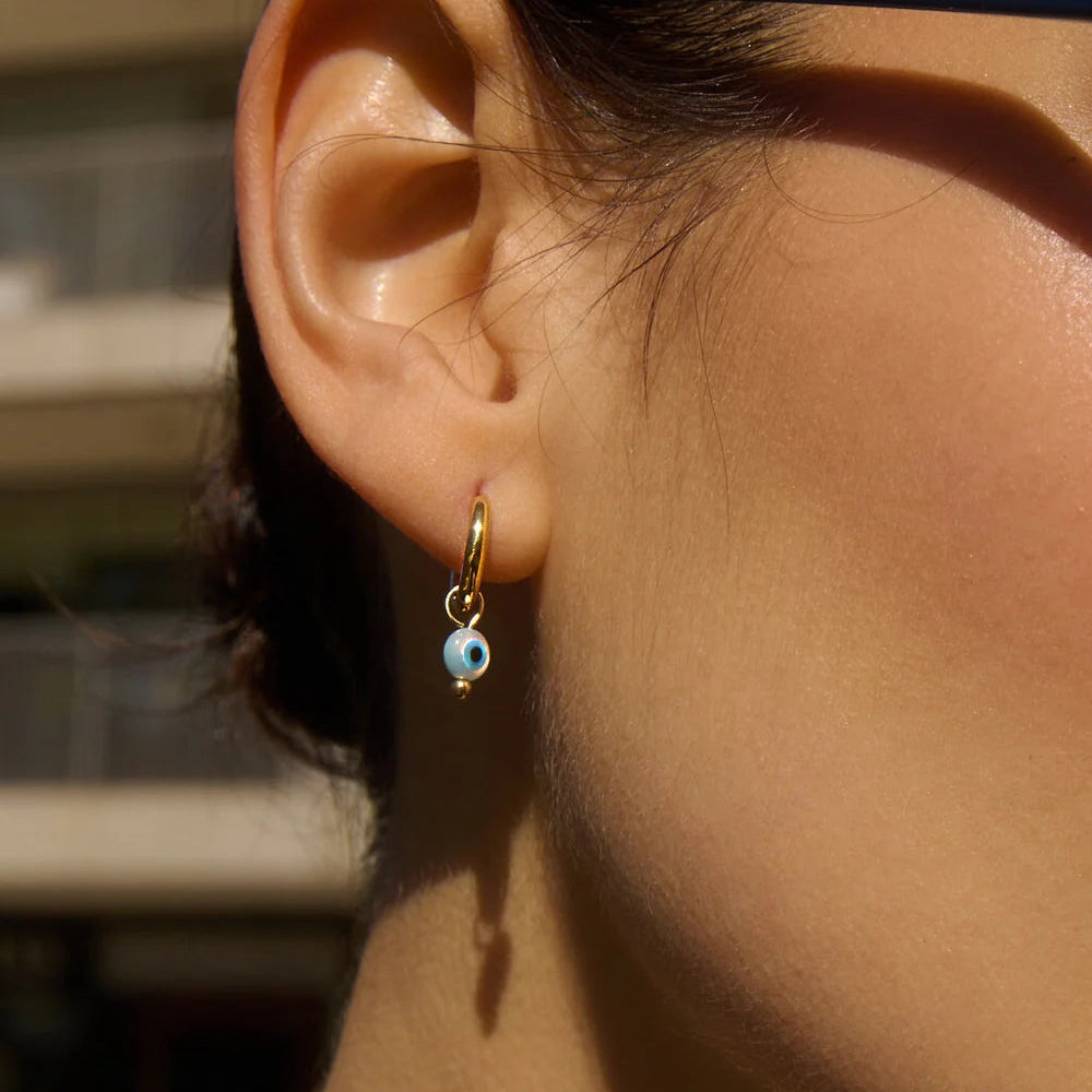 Evil eye pendant on a gold hoop earring.