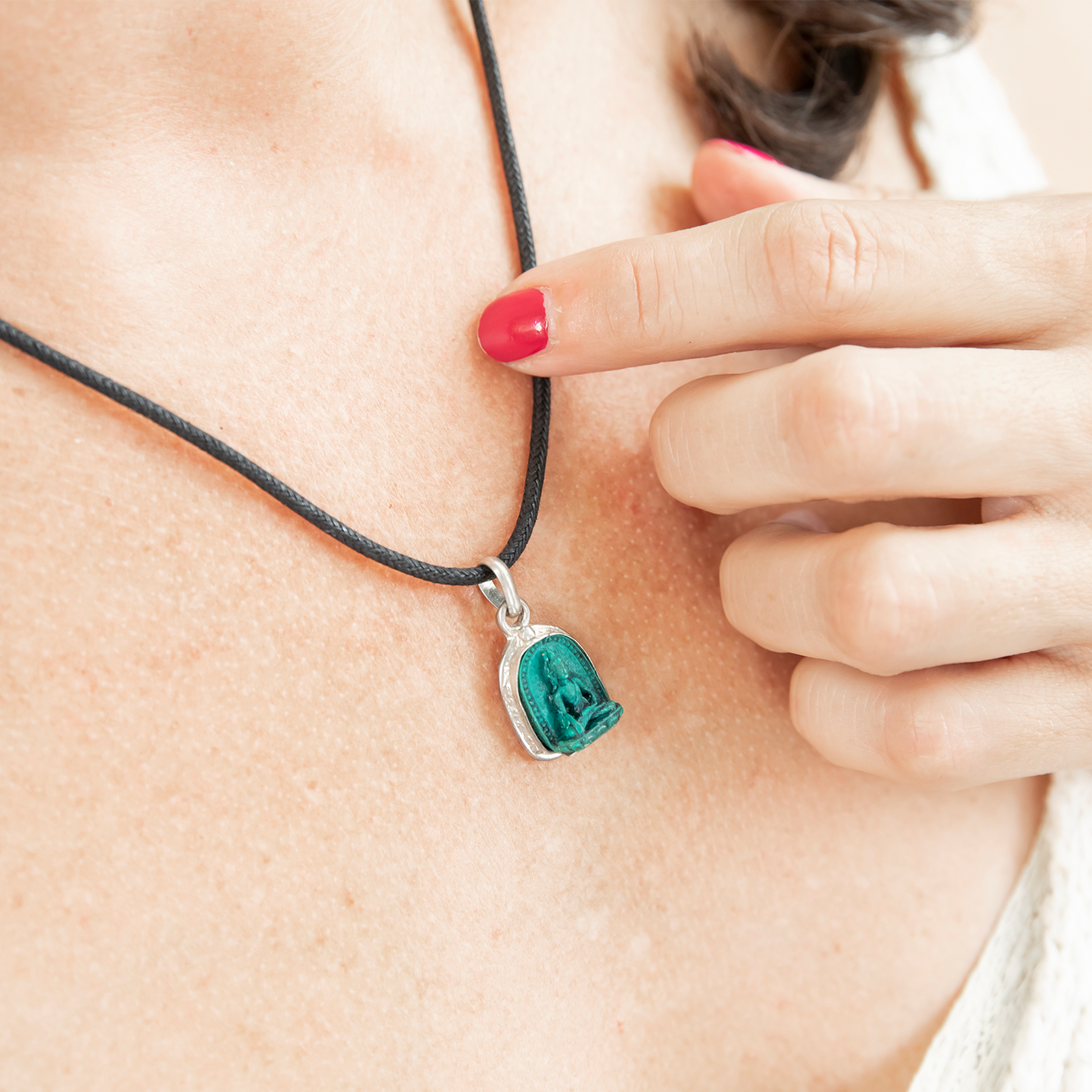 Close-up of Shakyamuni Pendant worn on a woman's chest. Her hand is in the photo, resting against her chest while her index finger lightly touches the cord of the necklace.