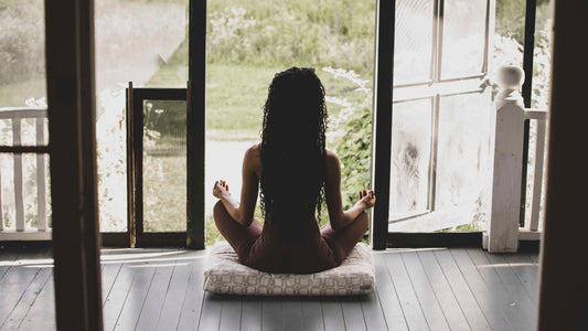 Woman meditating on a deck looking out a door.