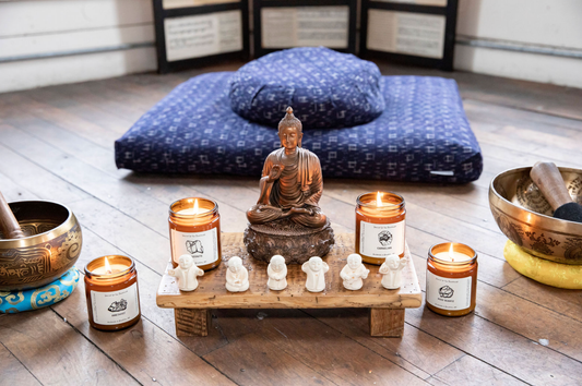 Altar with Buddha statues, surrounded by singing bowls and candles. There is a meditation cushion set in the background.