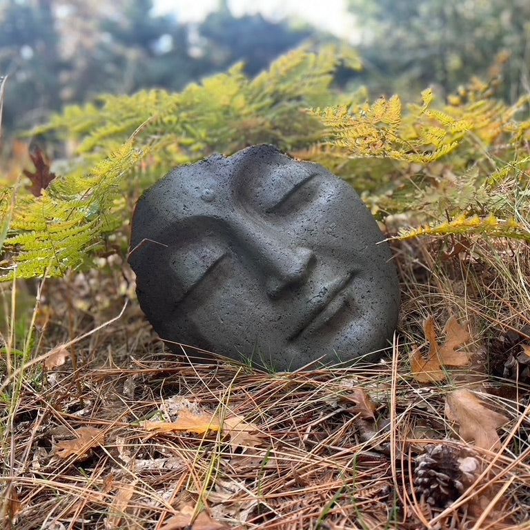Black stone with facial design in a forest setting
