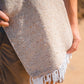Person holding a textured woven blanket with fringes on a blurred natural background
