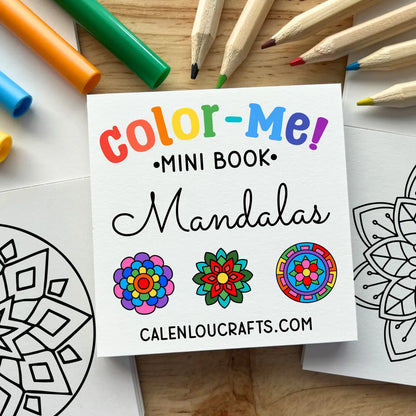 A square white booklet titled "color-Me! Mini Book: Mandalas" lies on a wooden surface, surrounded by colored pencils, markers, and partially filled coloring pages with mandala designs.