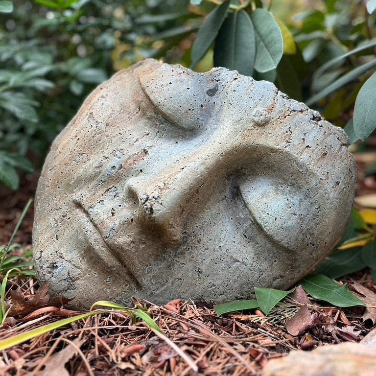 Concrete face sculpture on a natural ground with greenery