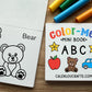 A children's mini ABC coloring book shown open on a wooden surface, alongside the front cover and colorful markers. The book features black-and-white bear illustrations on the inside pages and a colorful cover with the title 'Color-Me! Mini Book ABC' and the brand name CALENOUCRAFTS.