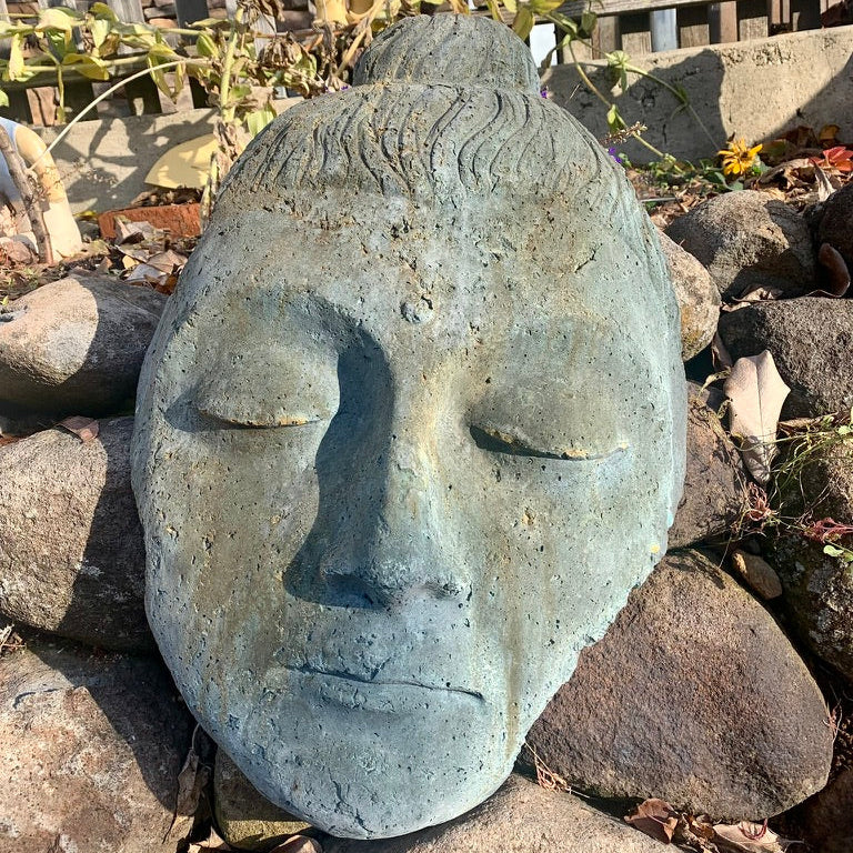 Stone face sculpture on a bed of rocks with a garden background