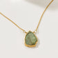 Gold necklace with a green stone pendant on a white background