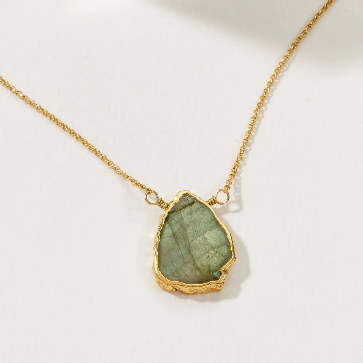 Gold necklace with a green stone pendant on a white background