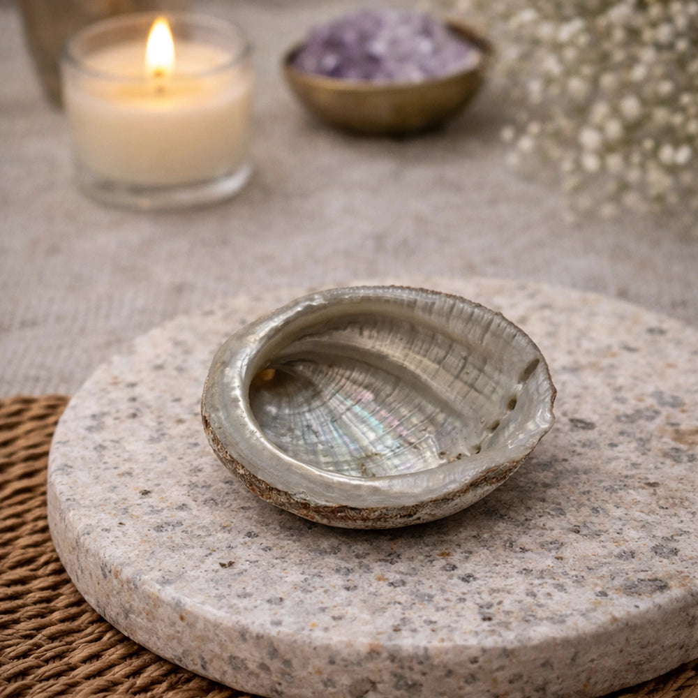 Abalone shell on a stone surface with a candle and amethyst stones in the background