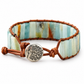 A beaded stretch bracelet featuring vertical rectangular stones in shades of light blue, mint green, and cream, wrapped in brown leather with a round silver tree-of-life charm.