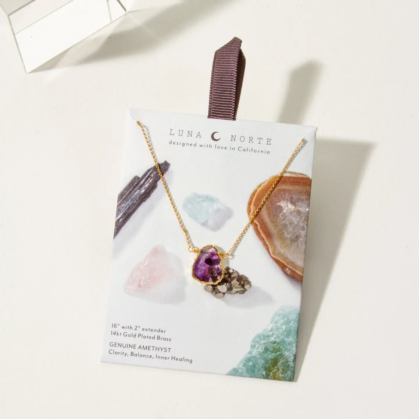 A gold-plated brass pendant necklace with a purple amethyst heart-shaped drop, displayed on a branded Luna Norte card against a clean white background.
