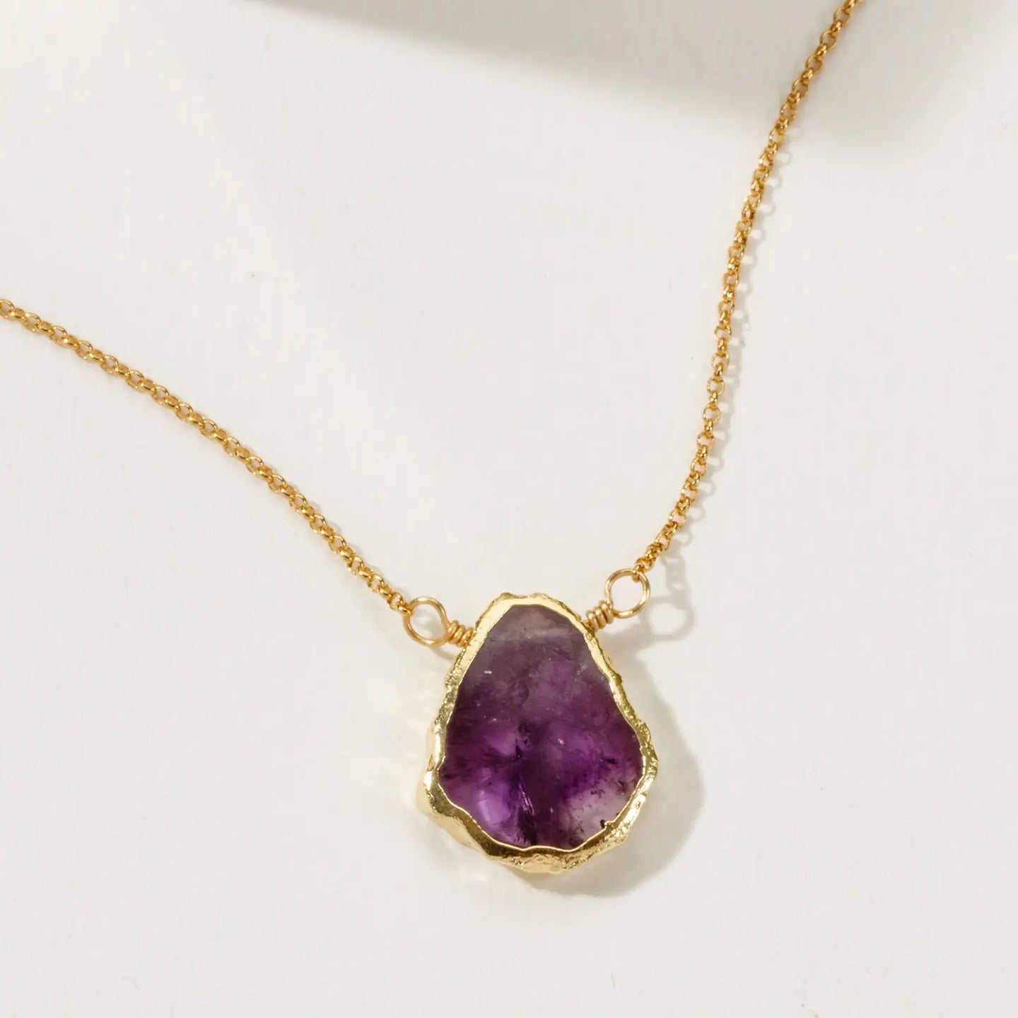 Gold necklace with a purple amethyst pendant on a white background