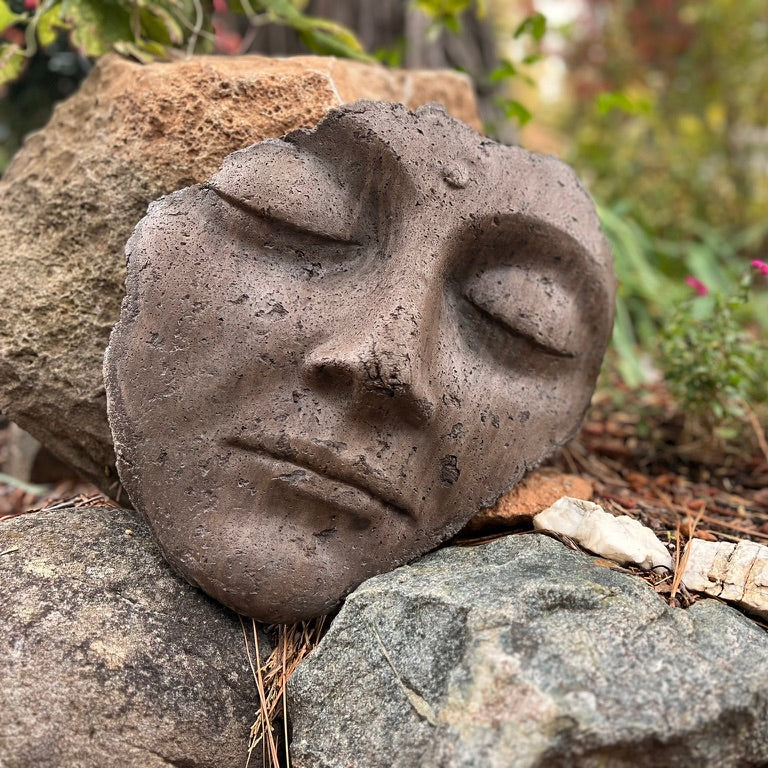 Stone face sculpture on a rocky surface with greenery in the background