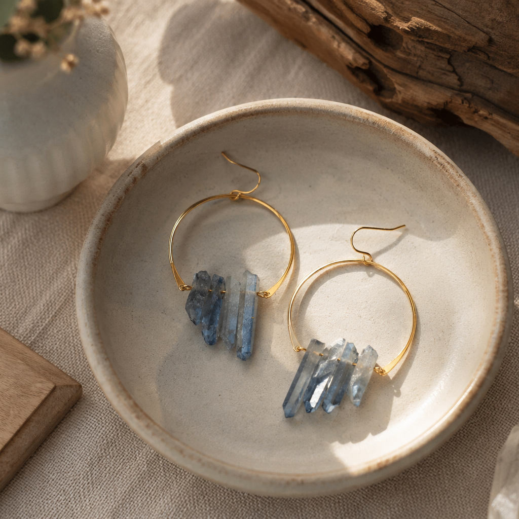 Gold hoop earrings with natural blue crystal clusters, displayed on a ceramic dish on a linen surface with boho-style props.