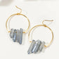 A pair of gold hoop earrings with clusters of natural gray-blue crystal points hanging from the hoops, displayed on a clean white background.