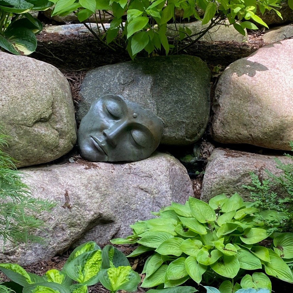 Decorative stone buddha face among green plants and rocks