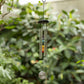 Decorative wind chime with colorful beads hanging against a green foliage background