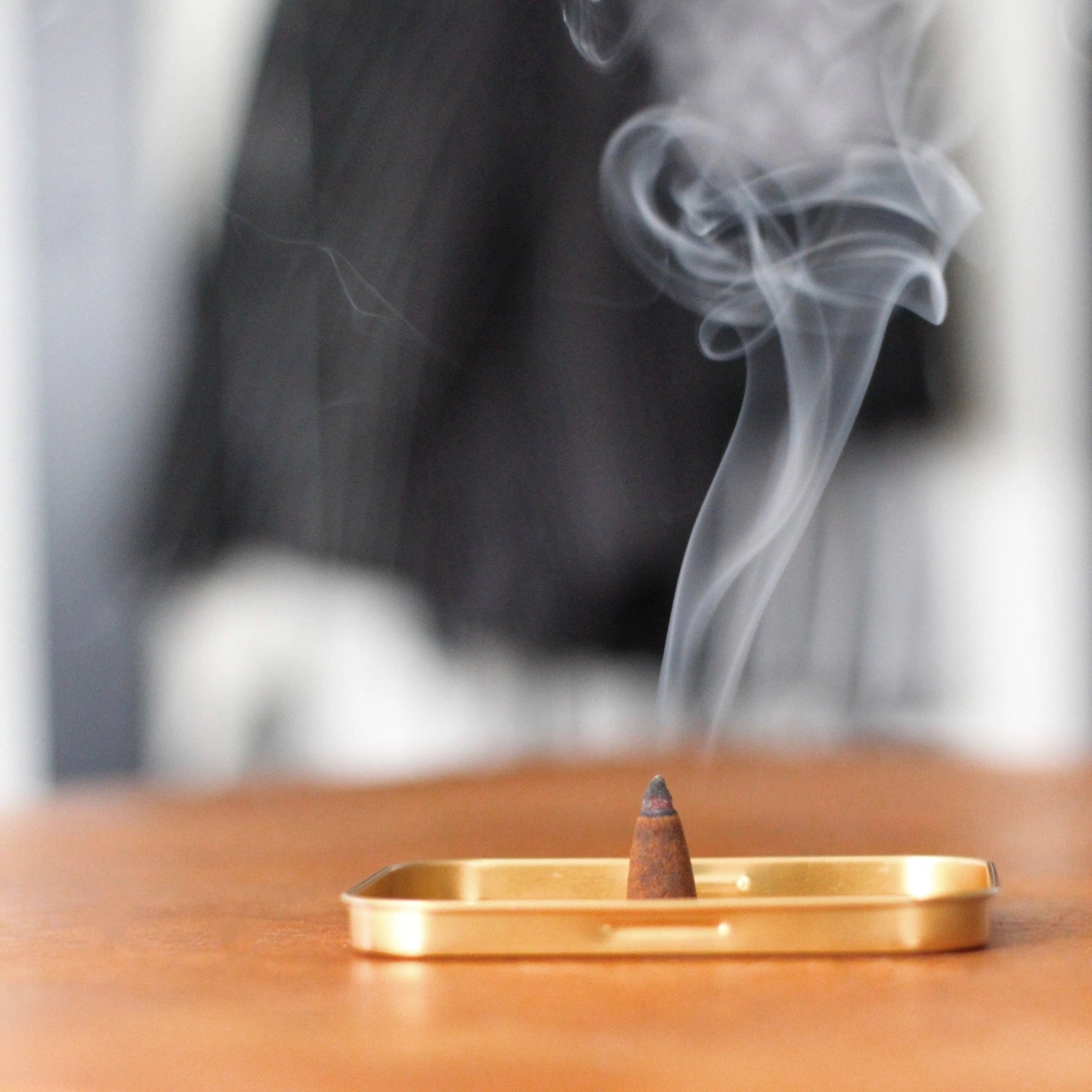 Incense cone burning on a brass tray with smoke rising against a blurred background