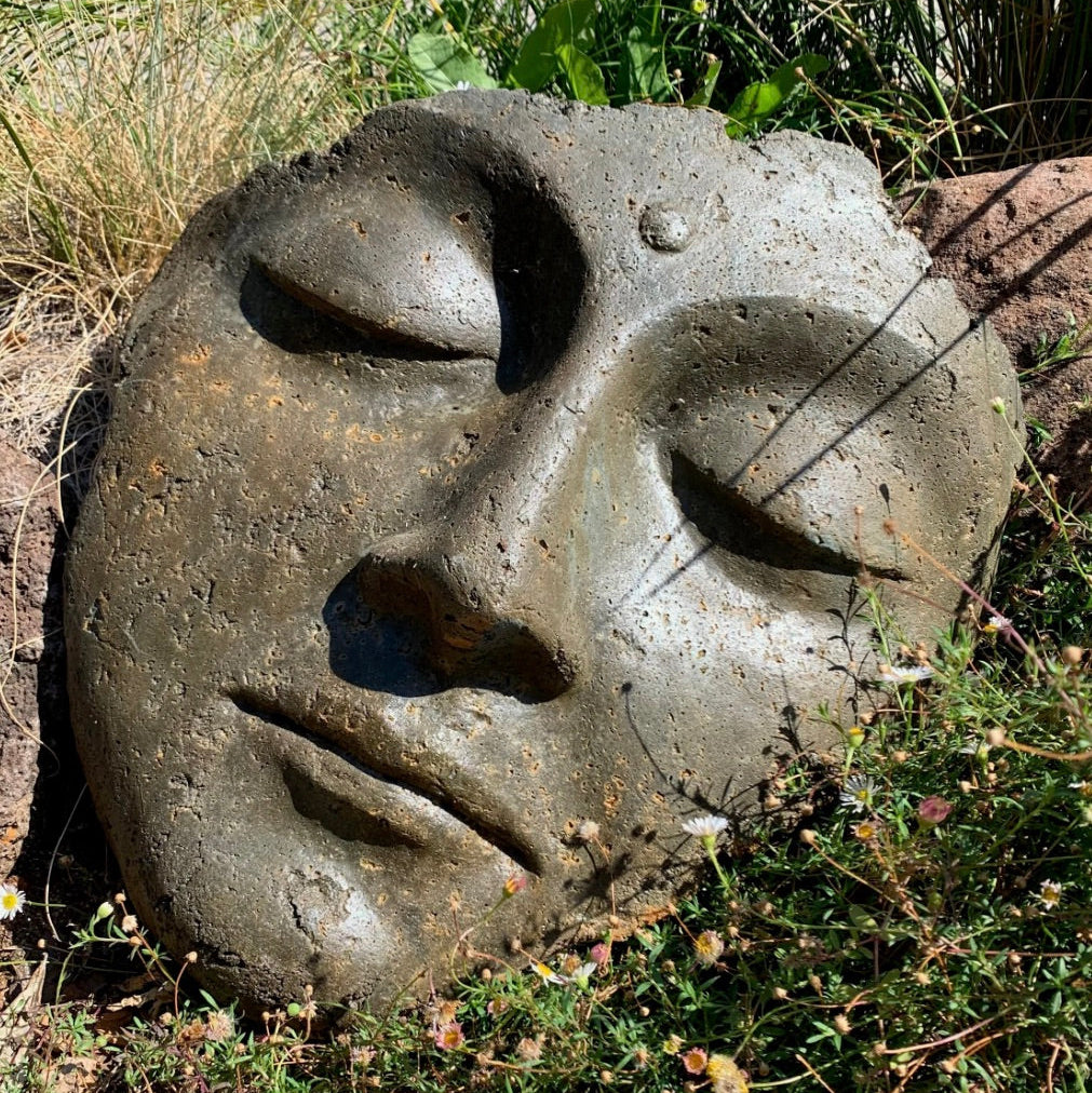 Concrete face sculpture in a natural setting with grass and rocks.