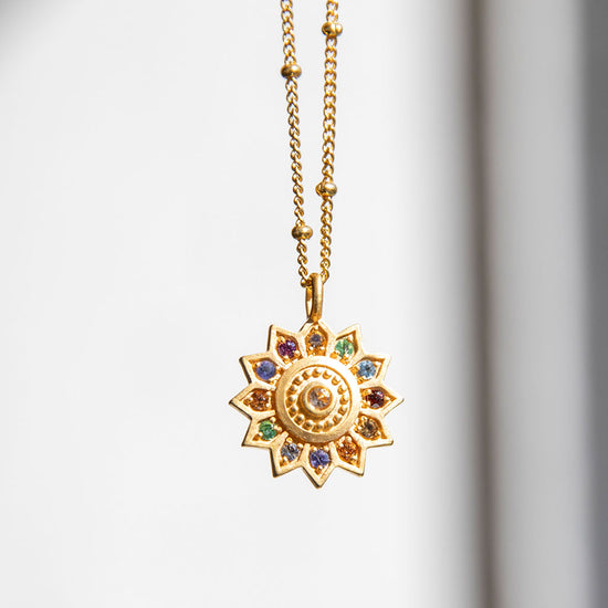 Gold sun pendant up against a white wall.