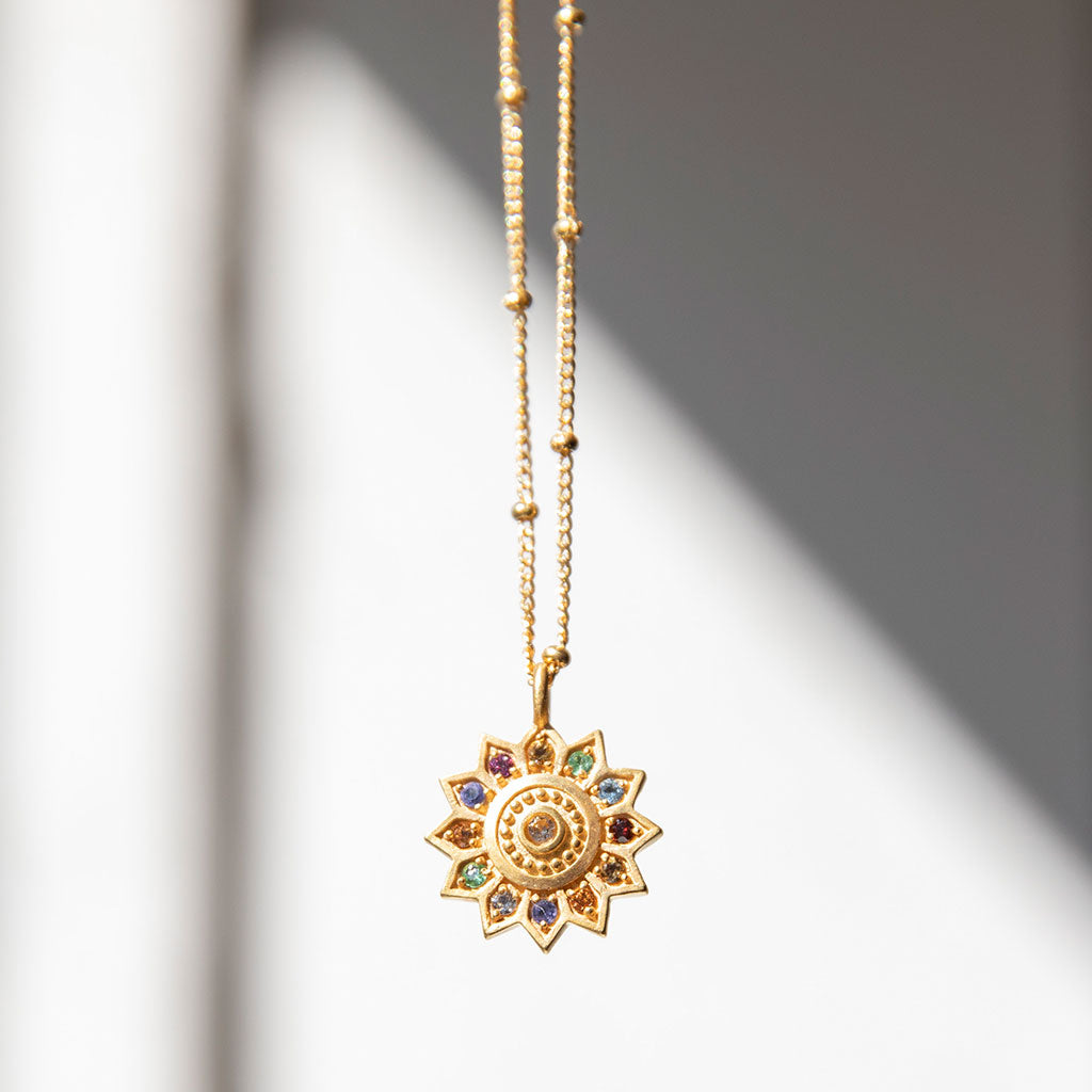 Gold necklace with pendant on a white wall.