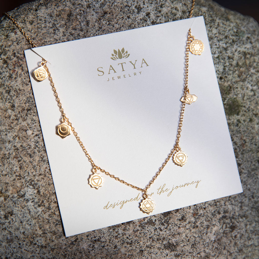 Gold chakra pendant necklace on a gray stone.