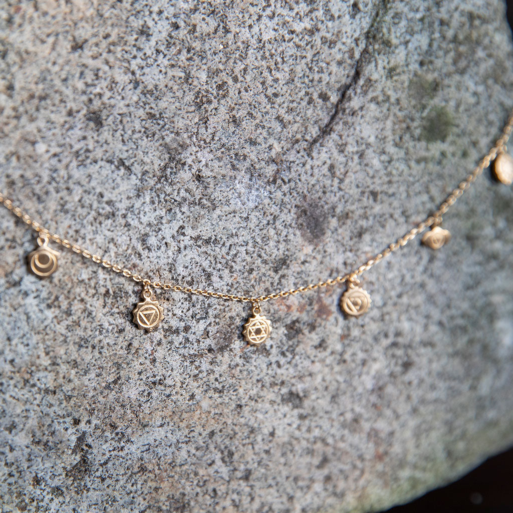 Gold chakra pendant necklace on a textured gray stone.