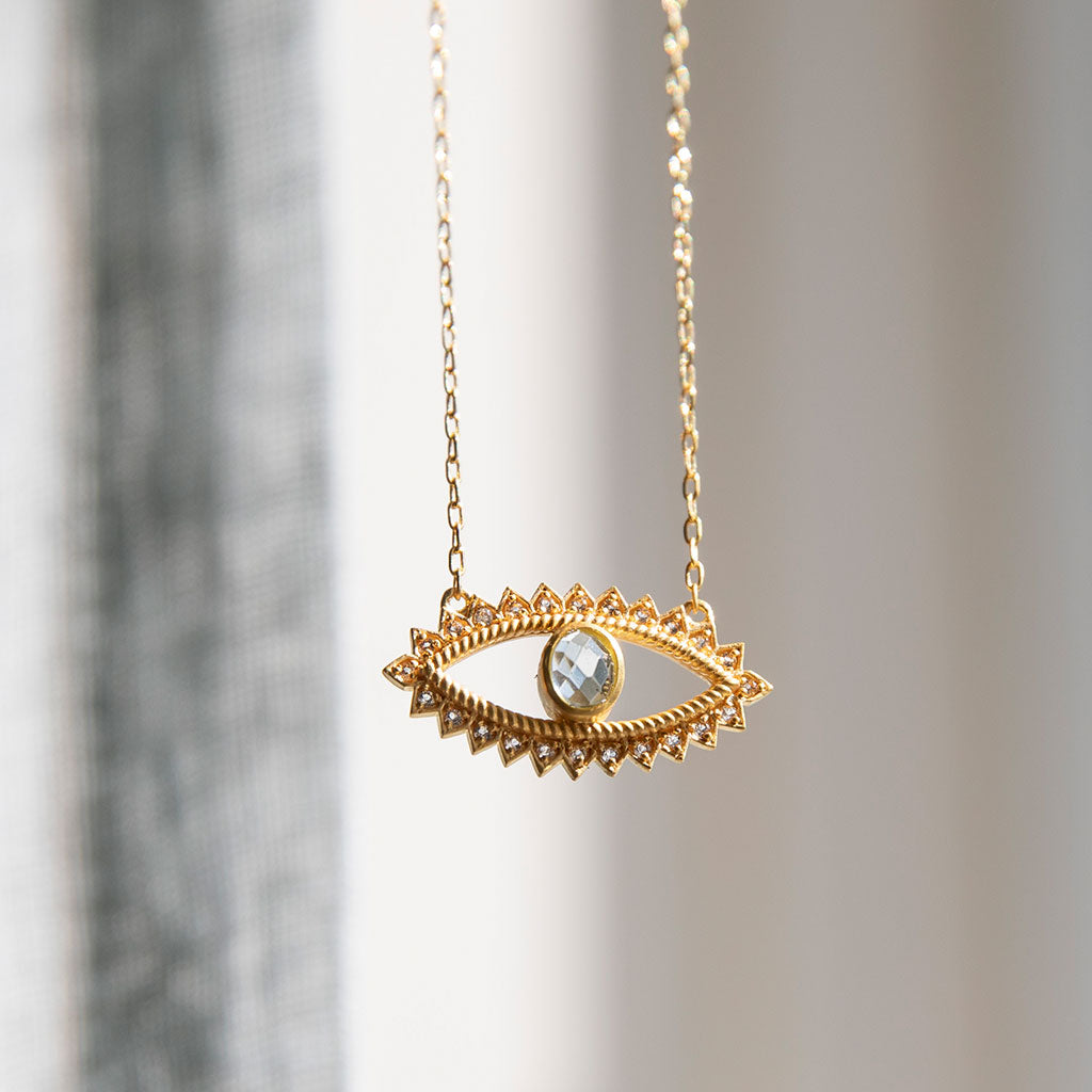 Gold necklace with eye pendant on a gry background.