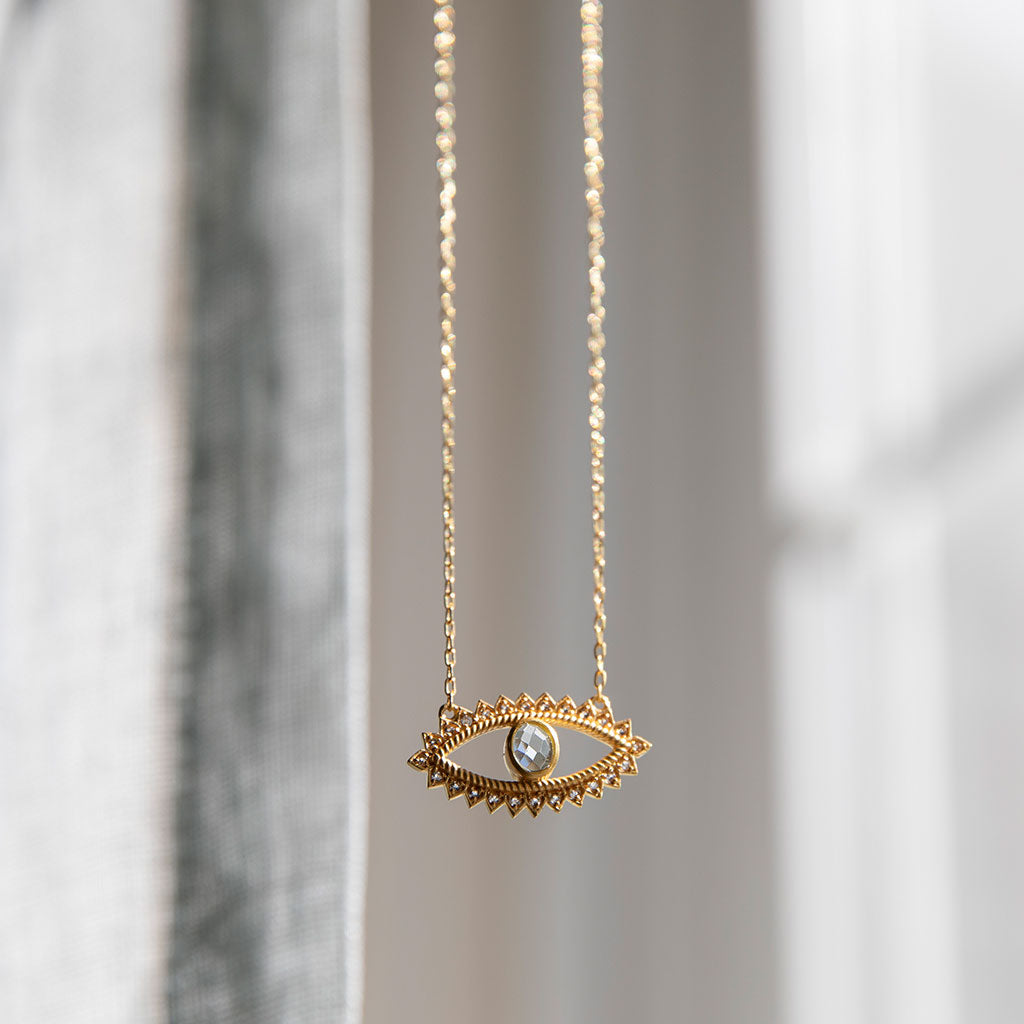 Gold necklace with eye pendant on a gray background.