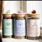 Three jars of herbal tea with labels and decorative stones on a light background