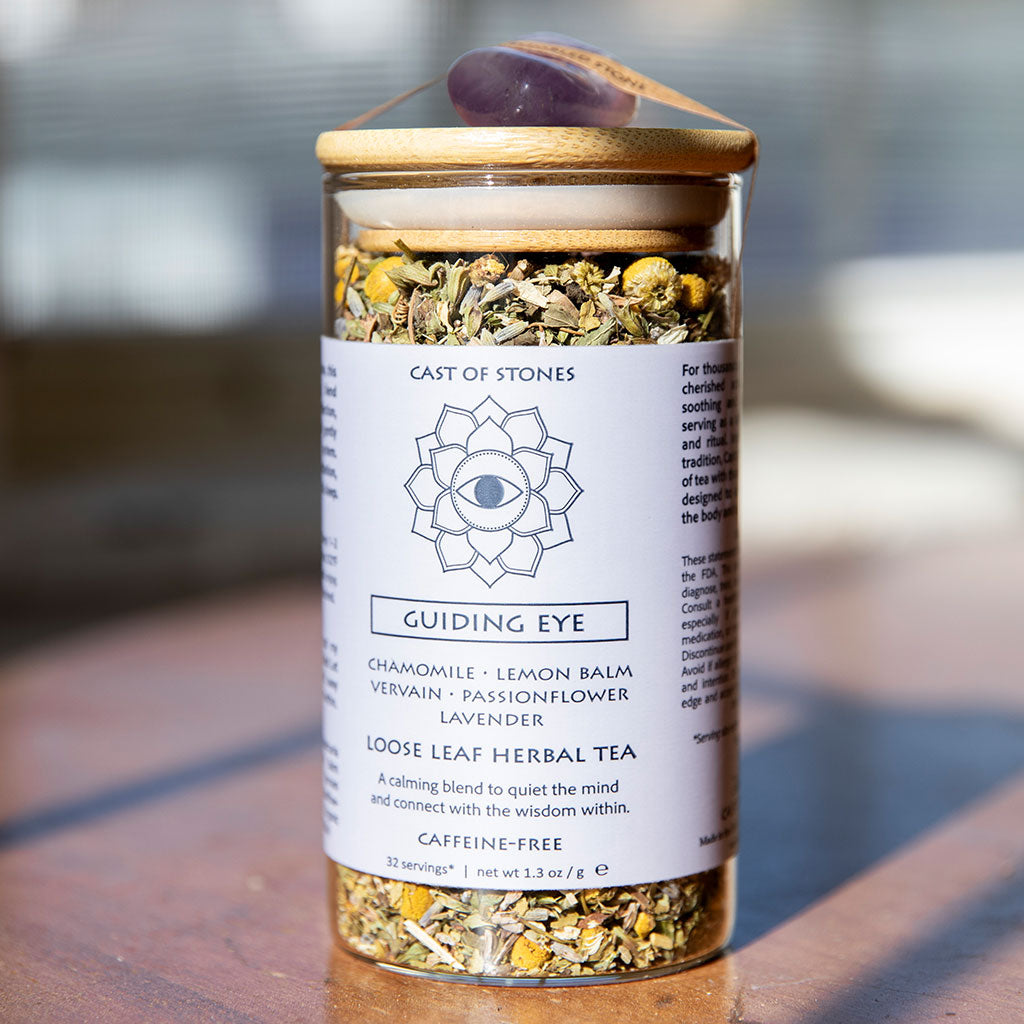 Glass jar of 'Guiding Eye' herbal tea with a wooden lid on a wooden surface.
