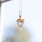 Crystal pendant on a gold necklace up against a blurry background.