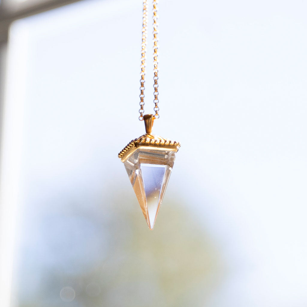 Crystal pendant on a gold necklace up against a blurry background.