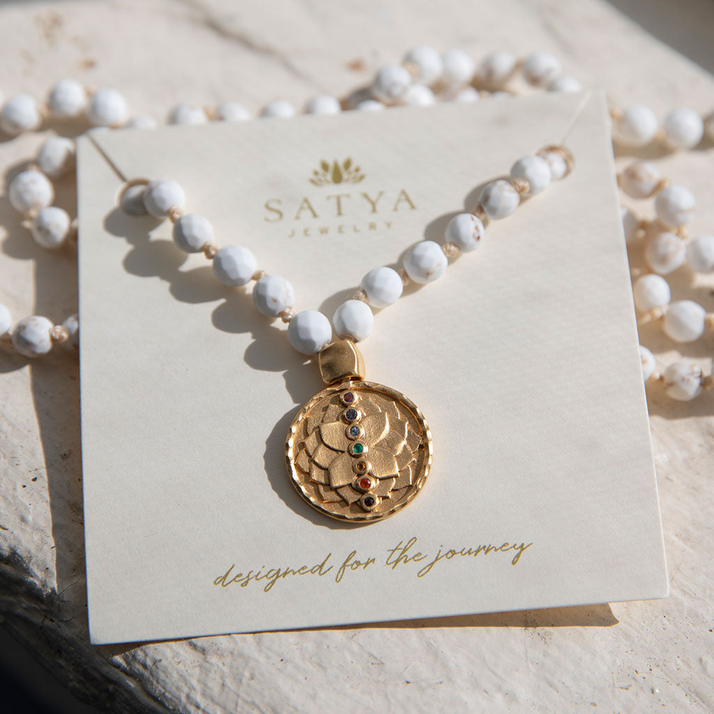 White turquoise mala with gold pendant on a shelf.