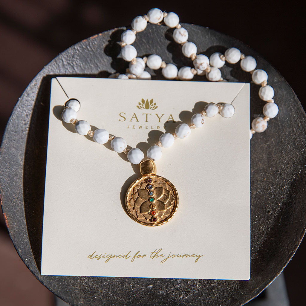 White turquoise mala with gold pendant resting on a wood bowl.