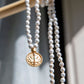White turquoise mala with gold pendant hanging on a wood beam.