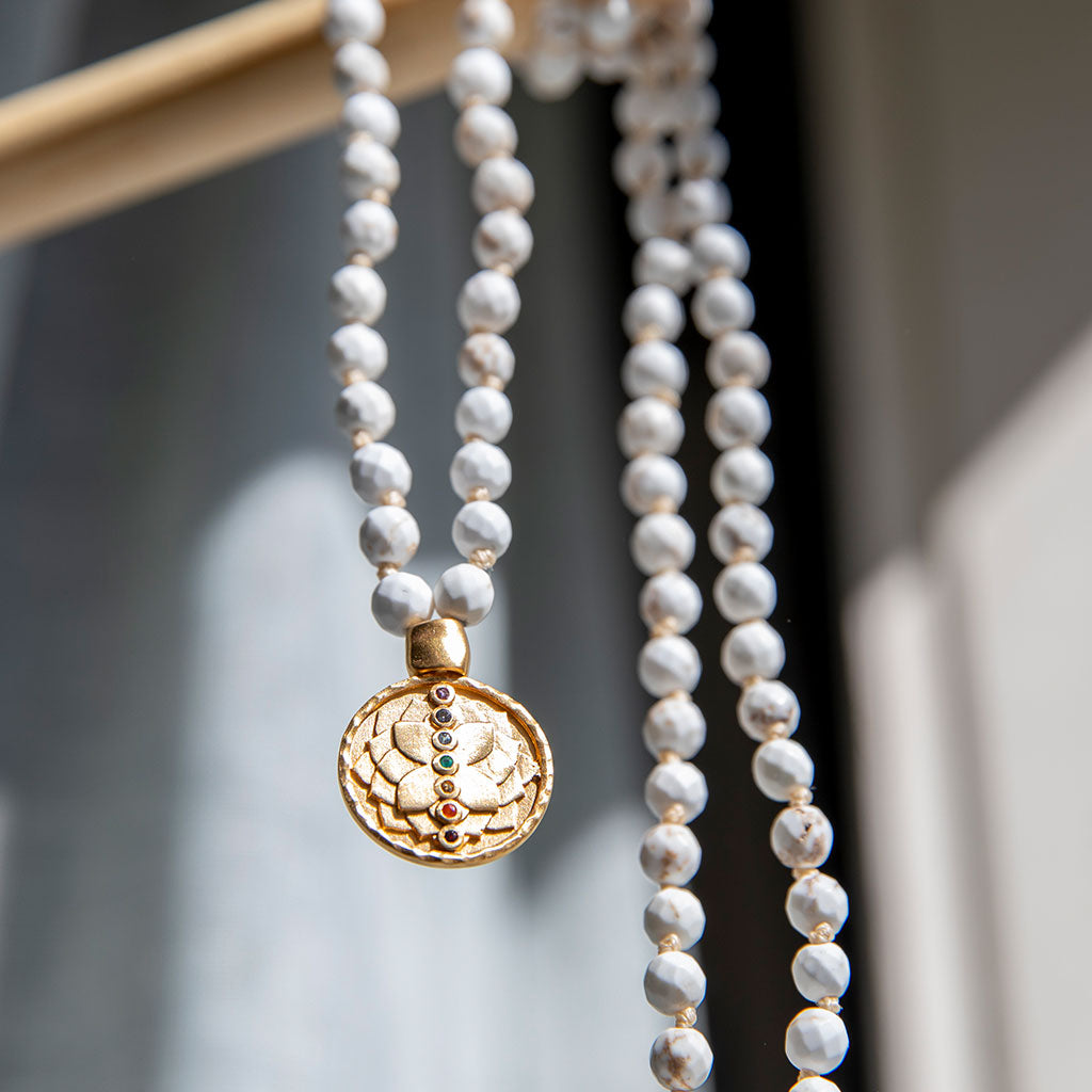 White turquoise mala with gold pendant hanging on a wood beam.