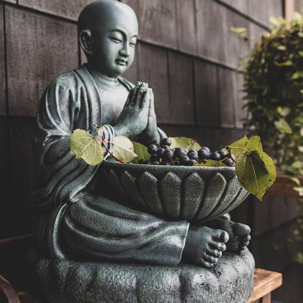 A statue of a Buddhist monk with an alms bowl, crafted from stone, with a weathered grey finish.