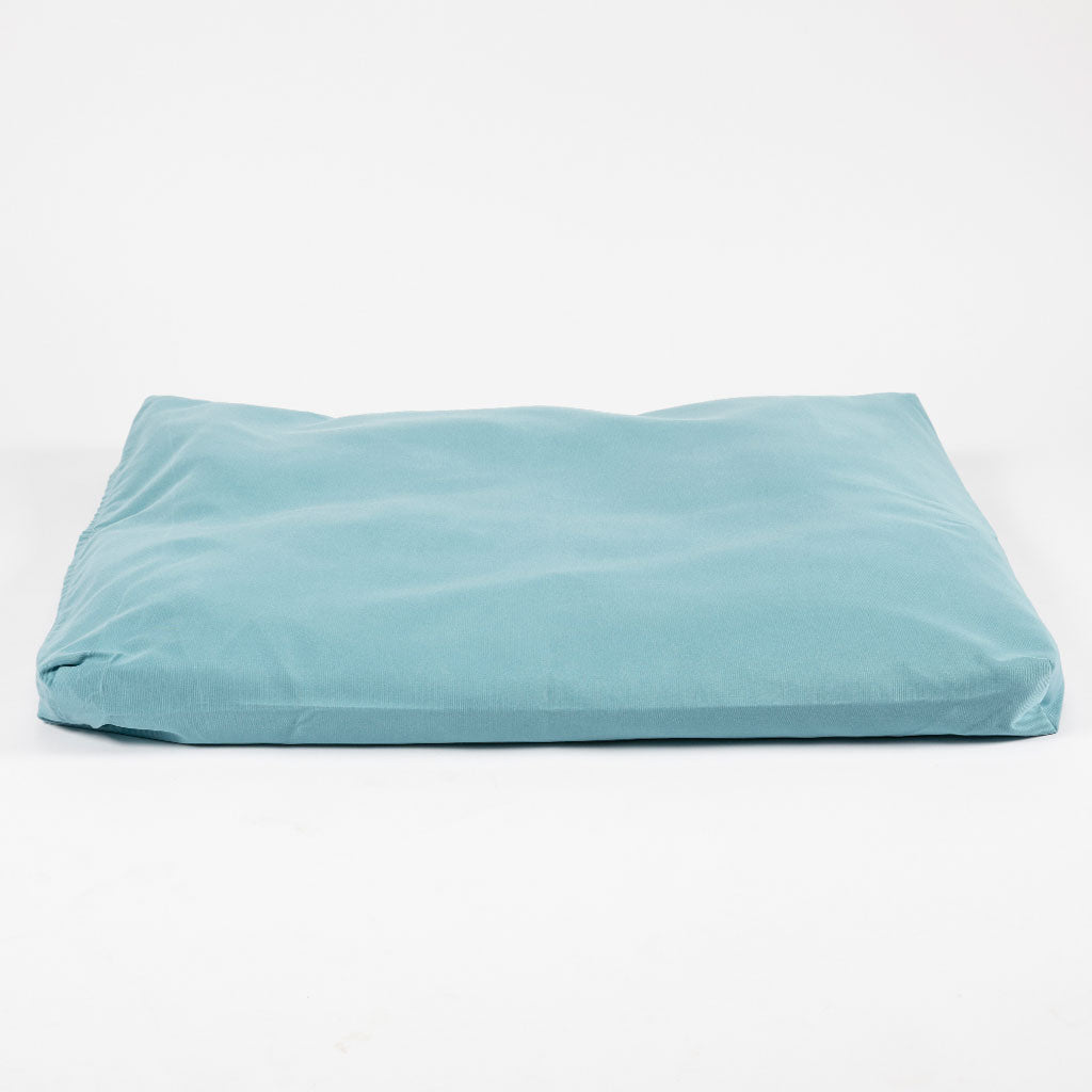 A rectangular, low-profile floor cushion in a light teal blue fabric, photographed against a seamless white studio background.