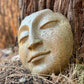 Stone face sculpture against a tree trunk in a natural setting
