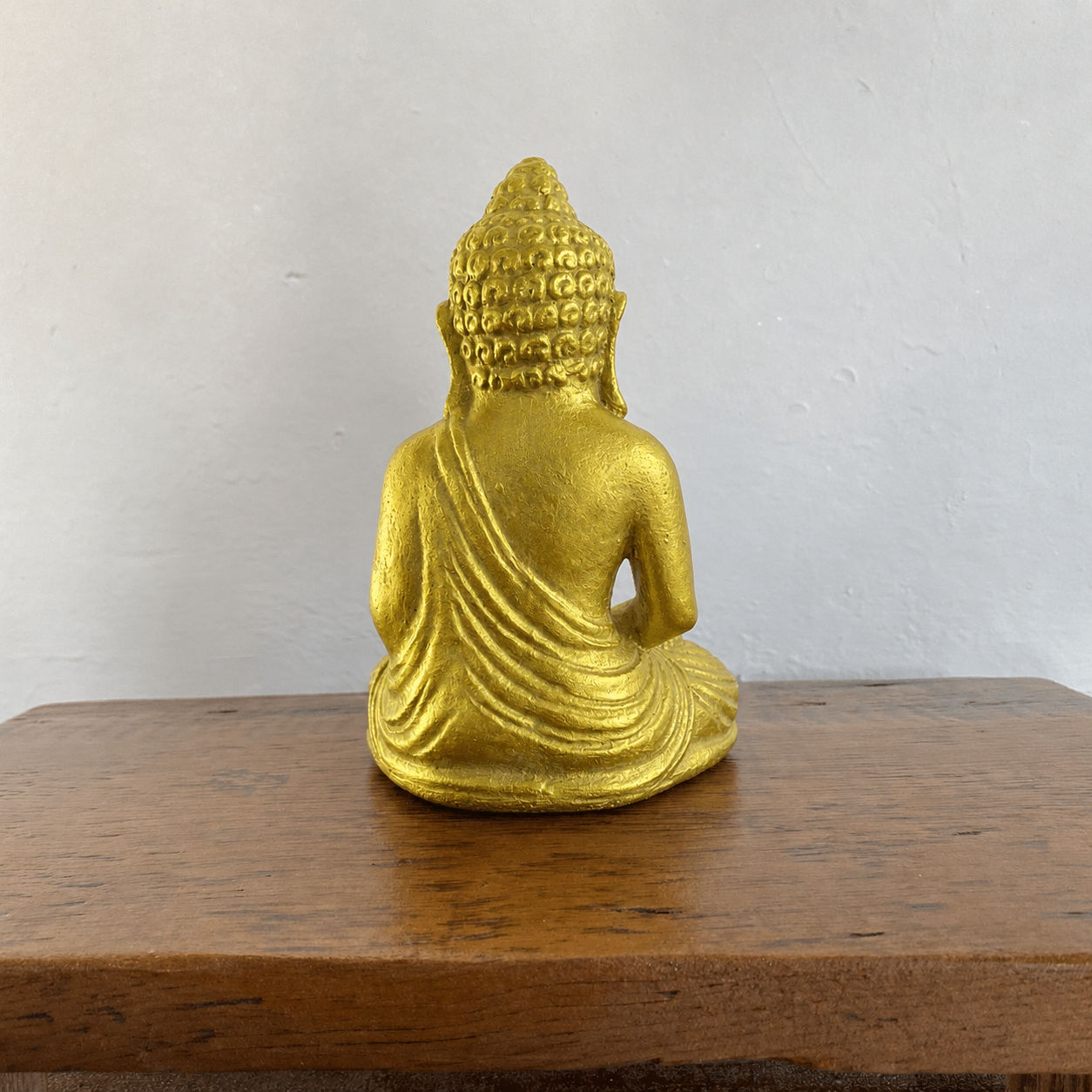 Gold Buddha statue on a wooden surface with a white wall background