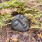Stone sculpture of a face on a forest floor with ferns and leaves