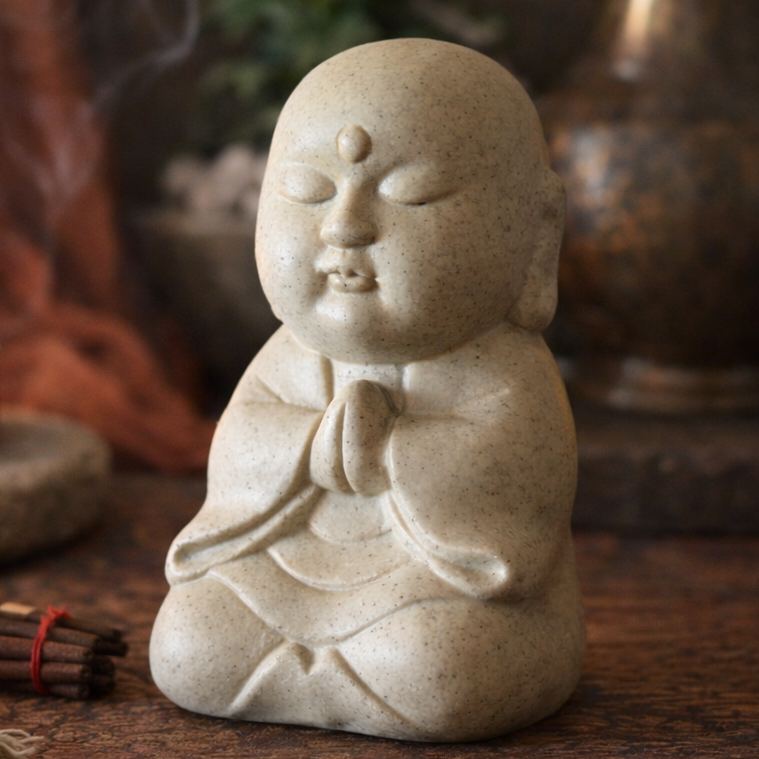 Stone statue of a meditating figure on a wooden surface with a candle and incense in the background.