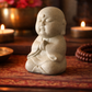 Stone statue of a meditating figure on a wooden surface with candles and flowers in the background