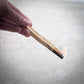 Hand holding a wooden matchstick with a small flame against a light background