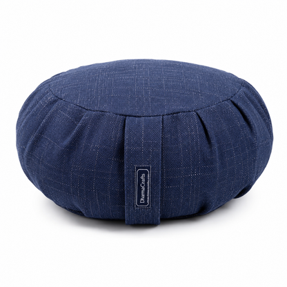 A round navy blue fabric cushion with a subtle woven texture and a central strap featuring a vertical label that reads 'DharmaCraft'. The cushion is photographed on a clean white background with a soft shadow underneath.