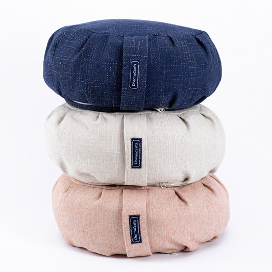 Three round, quilted cushion-like products stacked vertically on a white background, in navy blue, light beige, and blush pink. Each has a small fabric tag with the brand name 'Bloomsoft'.