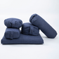 A set of five navy blue fabric yoga props, including a rectangular floor cushion, three cylindrical bolsters, and two round support pillows, arranged on a seamless white background.