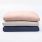 Three folded textured fabric cushions stacked vertically on a clean white background, in dusty pink, light beige, and navy blue.
